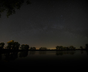Smooth surface of forest lake on a background of the night sky 
