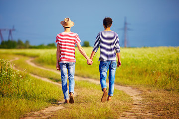 young male couple walking away on summer field path