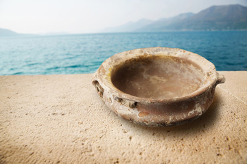 Ancient shallow bowl/Old ancient shallow bowl on stone table near seaside