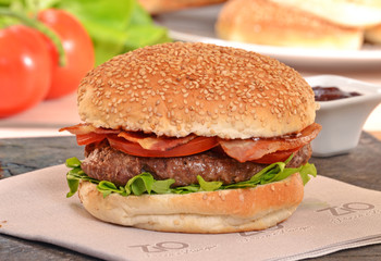 Hamburguesa con tocineta e ingredientes en la plancha.