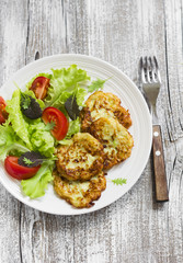zucchini pancakes and fresh vegetable salad on white plate 
