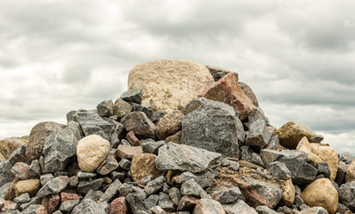 big pile of rocks and boulders piled in a heap under a grey dark cloudy sky in summer time