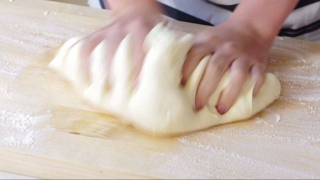 Hands boy knead pizza dough or bread on a wooden board with flour
