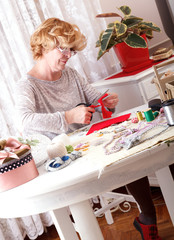 Senior women cuting red fabric with scissors to make ornaments