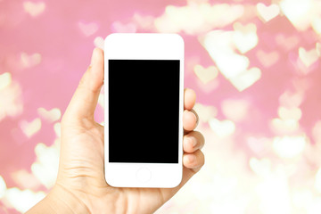 Hand holding smart phone on heart shaped bokeh pink defocused  b