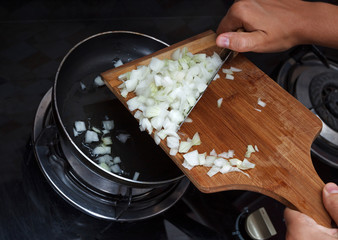 Hands drop chopped onions from board into pan