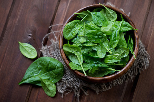 Top view of fresh spinach leaves in a bowl, dark wooden surface