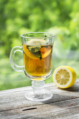 green tea with mint and lemon in a glass mug on a light wooden background