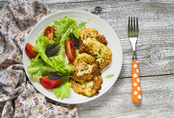 zucchini pancakes and fresh vegetable salad on white plate 