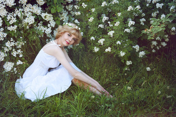 Beautiful blonde woman in white sundress sitting on the grass ne