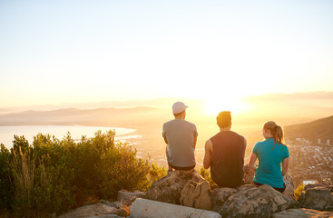 Friends sitting on a mountain trail watching the sunrise togethe