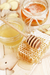 Glass cans full of honey, honeycombs and wooden stick on wooden background