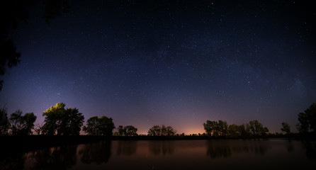 Smooth surface of forest lake on a background of the night sky 