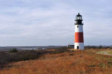Fototapeta na wymiar Sankaty Head Lighthouse Nantucket Cape Cod Massachusetts in the autumn with fall colors. It is a red and white striped light house on a bluff overlooking the sea. Copy space in the blue sky. 