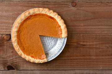 A pumpkin pie with a slice cut out. Horizontal format on a rustic wood table.  © Steve Cukrov
