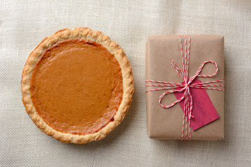 Obraz na płótnie Canvas High angle shot of a holiday pumpkin pie and plain paper wrapped present.
