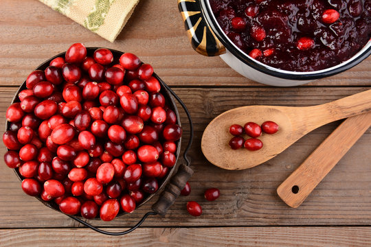 Overhead of a bucket of cranberries and a pot full of whole cranberry sauce on a rustic wooden table. Cranberry sauce is a traditional Thanksgiving side dish. Horizontal format.