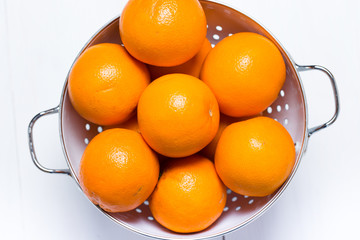 A vintage colander full of oranges on white wood