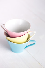 Three pastel colored china coffee cups on white wood