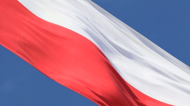 Nahaufnahme einer polnischen Flagge aus Stoff mit blauem Hintergrund und viel Wind.