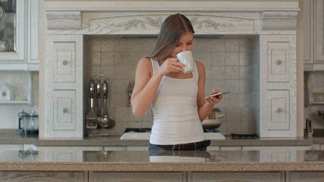beautiful happy young woman with phone drinking coffee at home