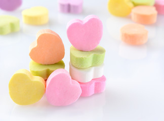 Closeup of candy Valentines hearts on a white reflective surface. Horizontal format with out of focus candies in the background.