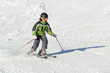 Fototapeta na wymiar The boy in a green jacket on skis in mountains