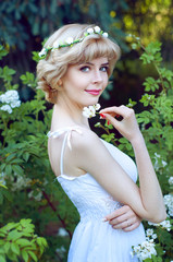 Beautiful blonde woman in white sundress posing in garden