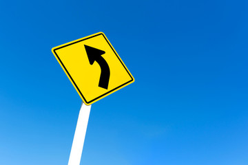 Yellow traffic left curve sign on blue sky background.