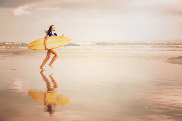 Beautiful sexy surfer girl on the beach at sunset running into