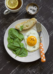 fried egg and fresh spinach on a white plate on a dark background