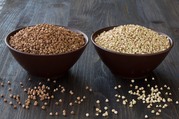 Green and brown buckwheat in ceramic bowls on a wooden surface