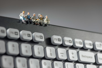 Miniature workers sitting on top of keyboard. Technology concept