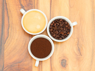 drei Tassen mit Kaffee, Kaffeebohnen und Kaffeepulver auf Holzti