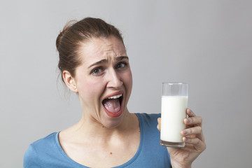 young woman scared of drinking a glass of smelly milk or disgusting white beverage