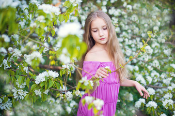 Beautiful toddler girl in pink dress posing in blossom flowers 