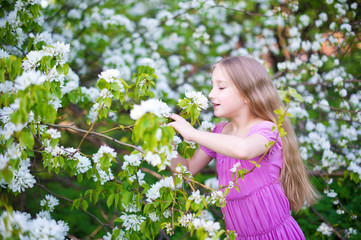 Beautiful toddler girl in pink dress stay in apple flowers 