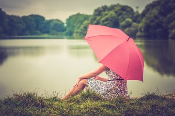 Young beautiful woman with red umbrella sitting near the pond -