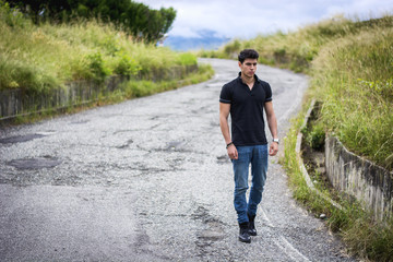 Fototapeta premium Young man in jeans and black t-shirt walking along rural road