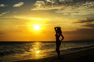 Silhouette of young woman on the beach at sunset sky