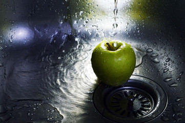 Green apple under the pressure of water in the kitchen sink