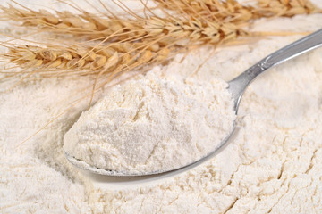 White flour in a spoon and ears of wheat