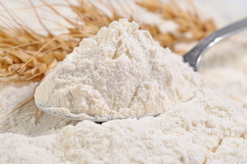 White flour in a spoon and ears of wheat