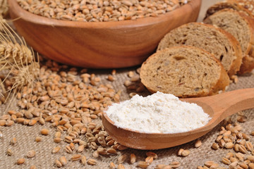 White flour in a wooden spoon, wheat and bread