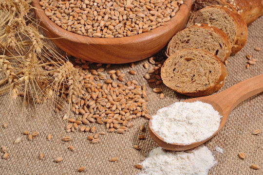 White flour in a wooden spoon, wheat and bread