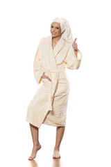 Fototapeta premium smiling woman in bathrobe and towel on her head showing thumbs up