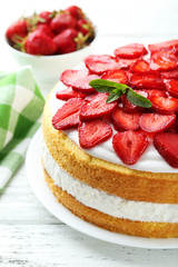 Sweet cake with strawberries on plate on white wooden background