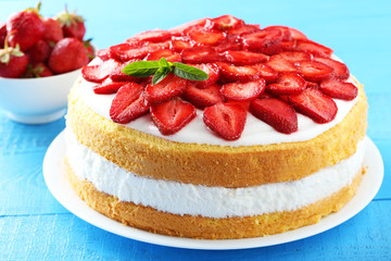 Sweet cake with strawberries on plate on blue wooden background