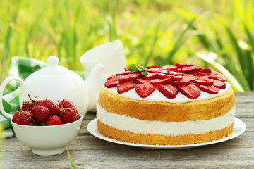 Sweet cake with strawberries on plate on grey wooden background