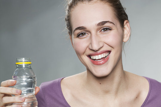 young beautiful woman wearing purple shirt smiling in showing a bottle of water